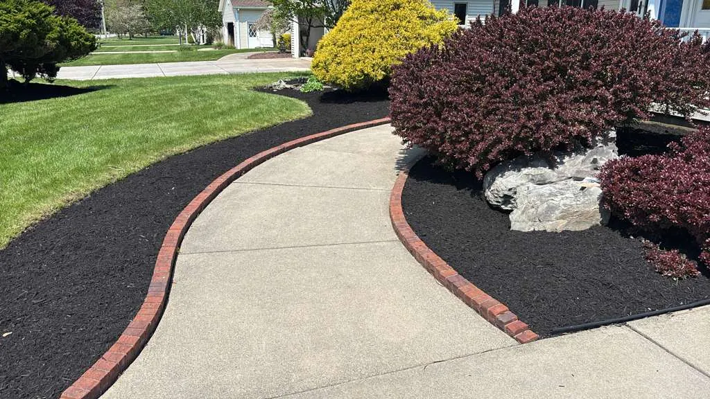 Brick-edged mulch bed following a driveway curve in Buffalo NY